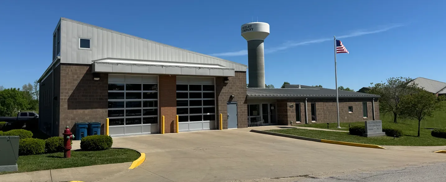 Modern civic building entrance with steps, ramp, landscaping, and American flag under blue sky